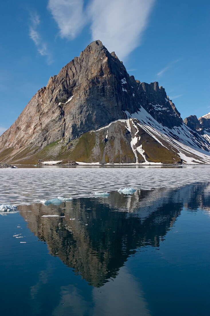 Ein zerklüftetes Gebirge wirft eine Reflexion in den schmelzenden Fjord darunter.