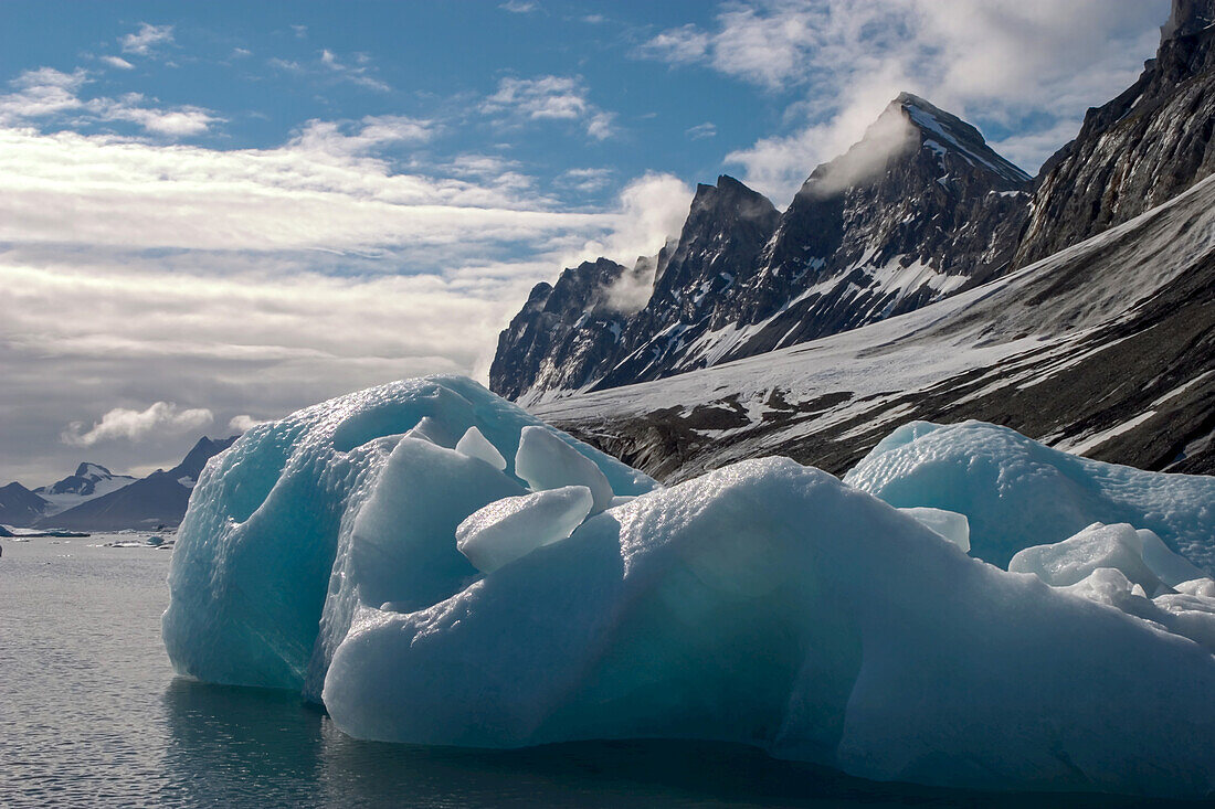 Blue ice, clouds, jagged mountains in an Arctic environment.