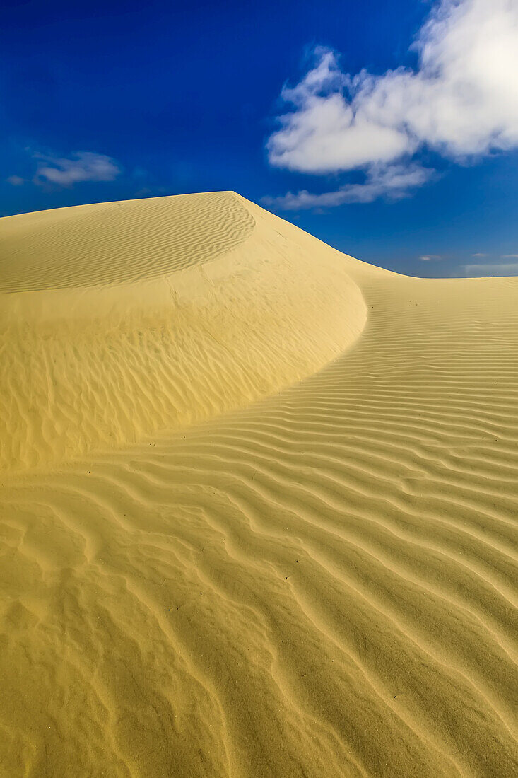 Eine Sanddüne mit Wolken und Windkräuseln.