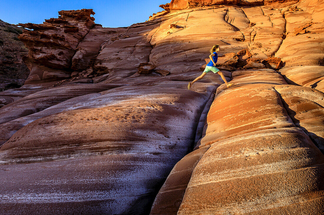 Ein Mädchen springt über Risse in einer roten Sandsteinformation auf der Baja Halbinsel, bei Puerto Gato.