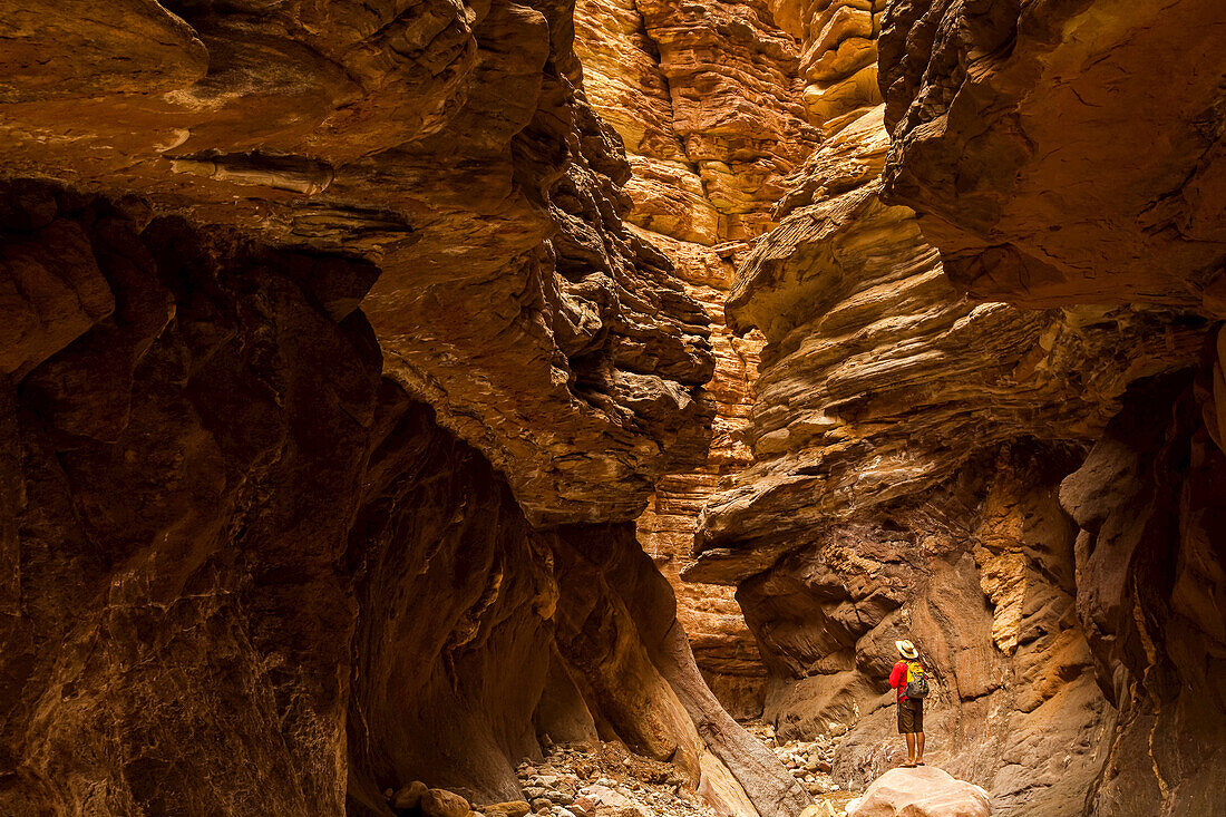 Hiker in a slot canyon observing sandstone layers and erosion.
