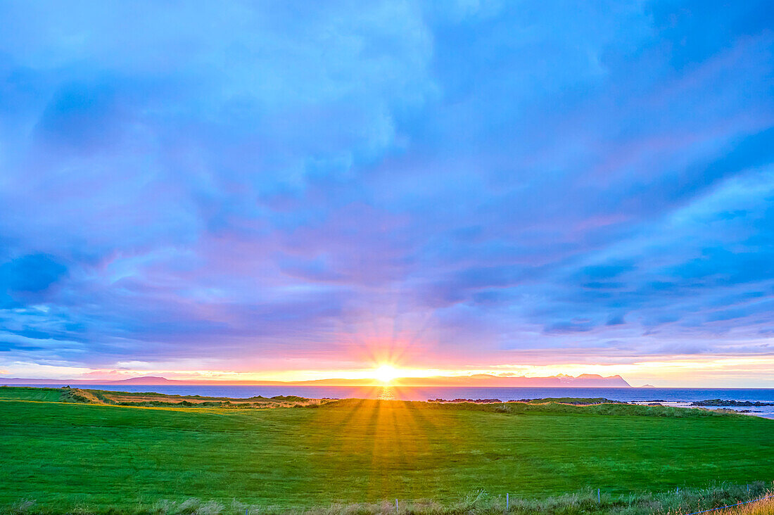 Atemberaubender Sonnenuntergang über den grasbewachsenen Feldern entlang der Küstenlandschaft des Nordatlantiks an der historischen Stätte von Illugastadhir auf der Halbinsel Vatnsnes in der nördlichen Region Islands; Vatnsnes Halbinsel, Nordurland Vestra, Island