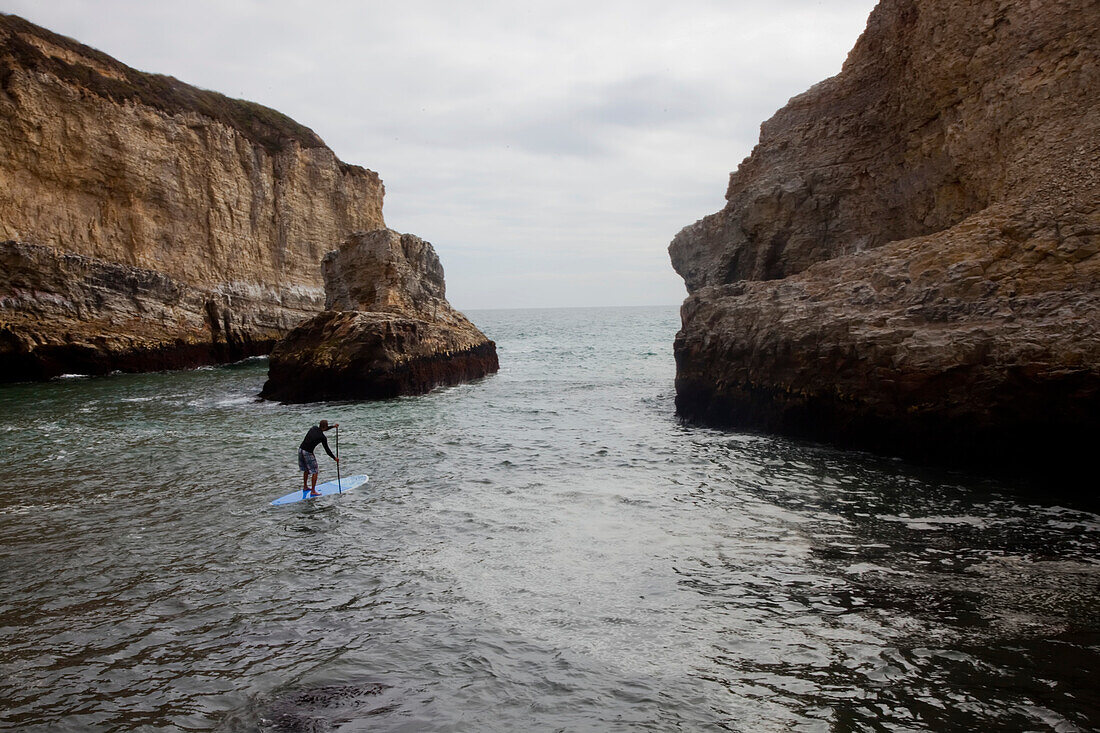 A stand up paddleboarder off the rough coastline north of Santa Cruz.