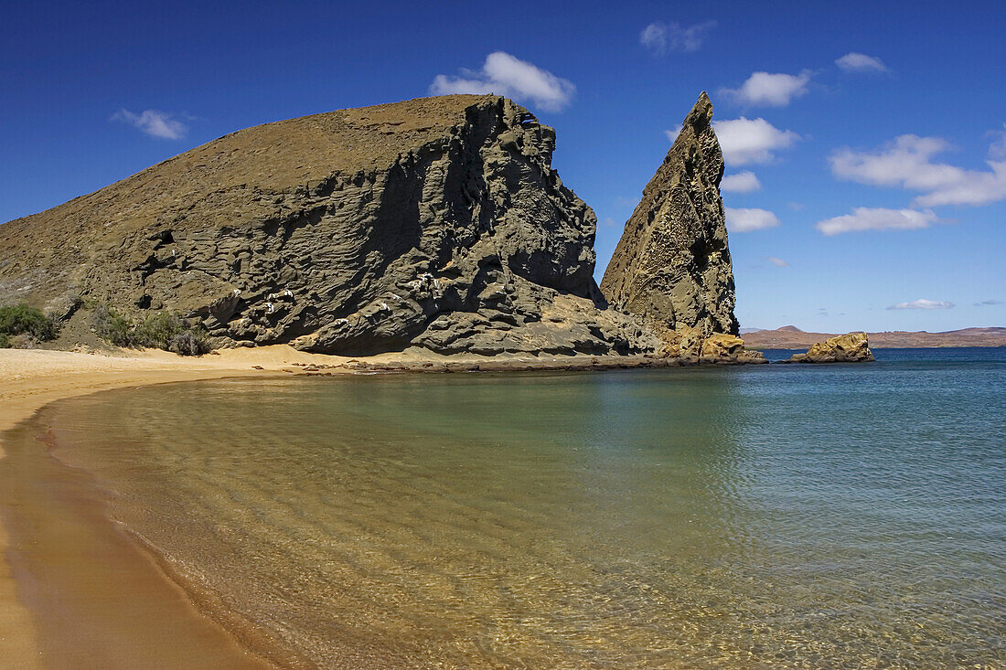 Friedlicher Strand mit ruhigem Wasser in der Nähe einer zerklüfteten Felsformation.