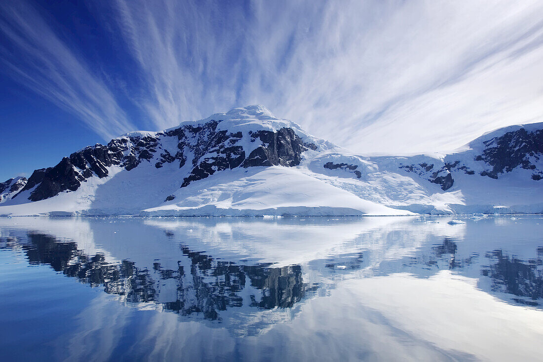 Cirrus clouds over mountainous coast, and reflection in water.