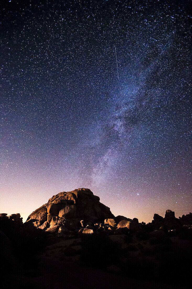The milky way in a starry night sky over a granite dome; Joshua Tree National Park, California, United States of America