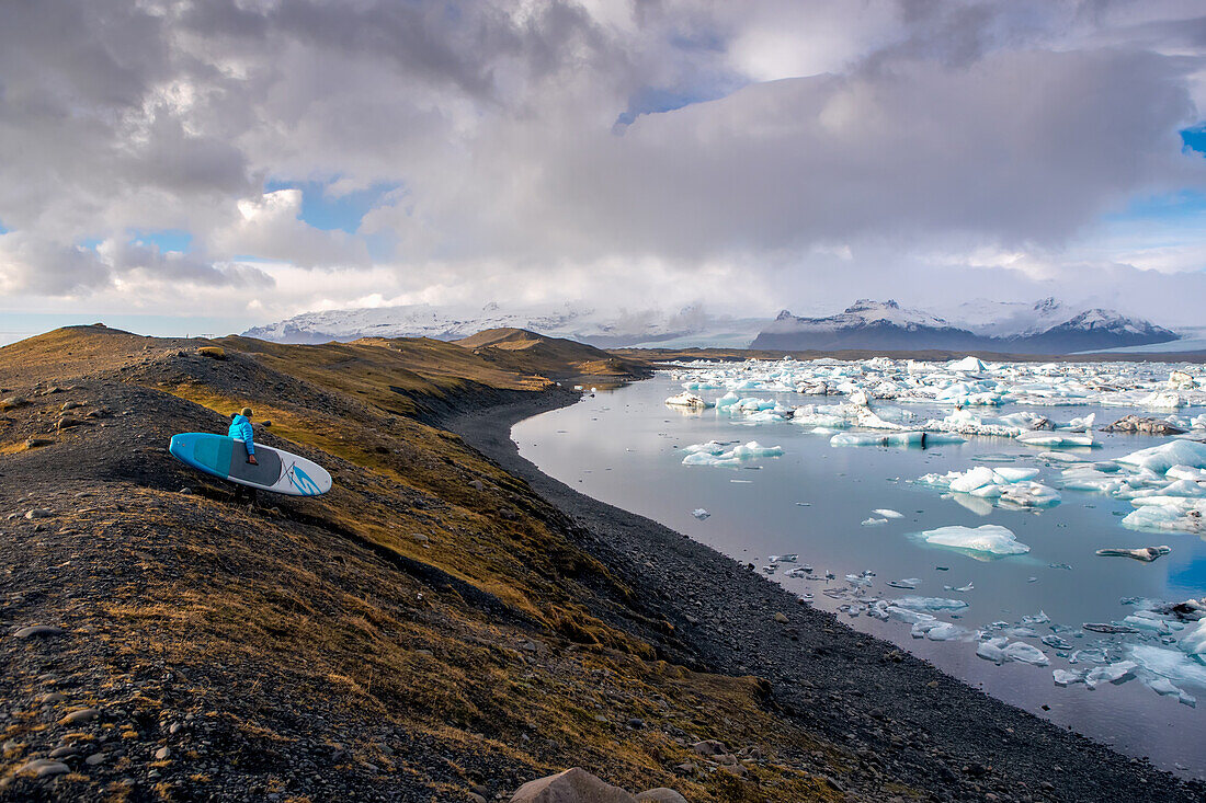 A man walking a paddleboard down to the Jokulsarlon glacier lagoon.