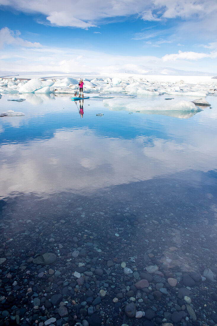 A woman on an inflatable paddleboard paddling on the Jokulsarlon glacier lagoon.