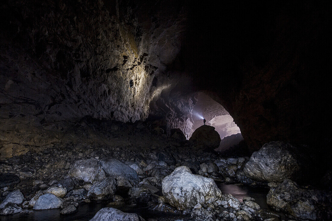 A man stands on a boulder and shines his headlamp onto the walls of a cave in China.