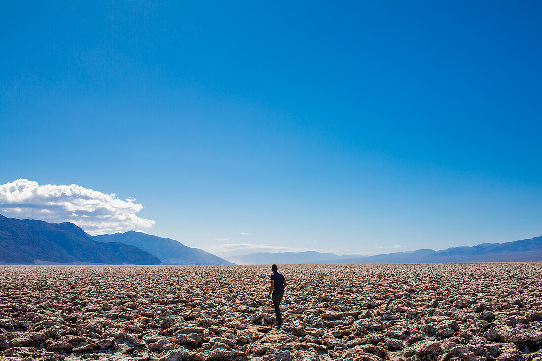 A man walking across the cracked desert plains in Death Valley.