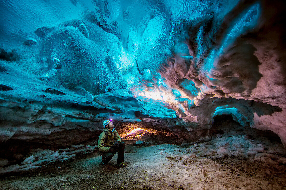 A man looking up at the ice in a glacier cave.