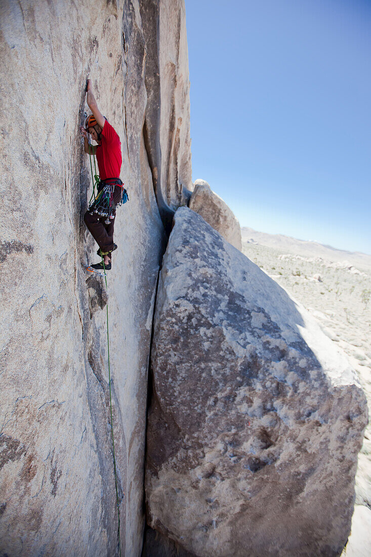 Ein Trad-Kletterer klettert einen flachen Riss in einer vertikalen Granitwand.