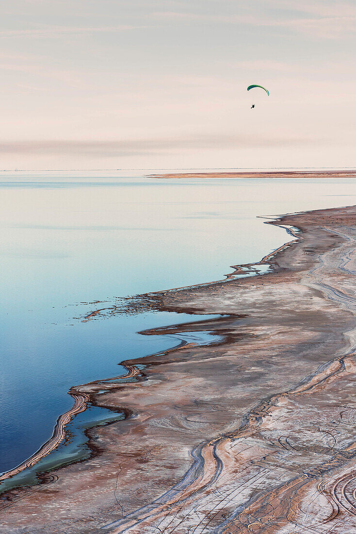 A paramotorist flying along the shore.