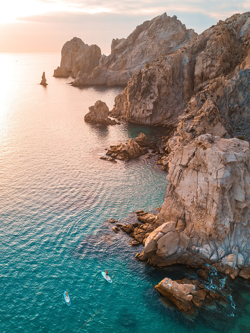 Luftaufnahme von Paddelboardfahrern entlang der felsigen Küste am Ostkap von Cabo bei Sonnenuntergang; Cabo San Lucas, Baja California Sur, Mexiko