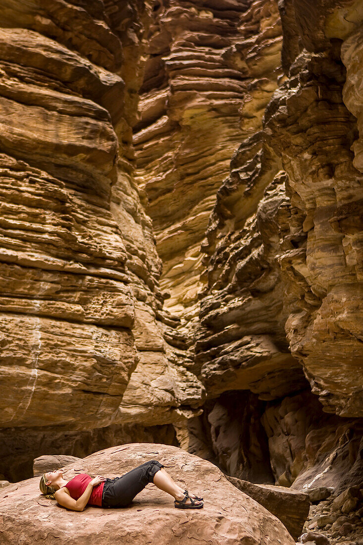 Ein Wanderer entspannt sich auf einem großen Felsen im Blacktail Canyon am Colorado River Mile 120 beim Arizona Highways Photography Workshop; Grand Canyon National Park, Arizona, Vereinigte Staaten von Amerika