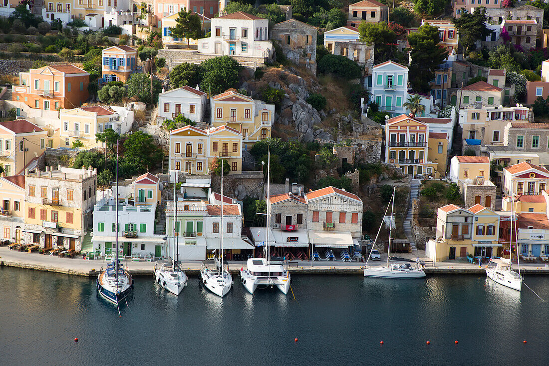 Overview of pastel colored buildings and sailboats moored along the seawall at Gialos Harbor, Symi (Simi) Island; Dodecanese Island Group, Greece