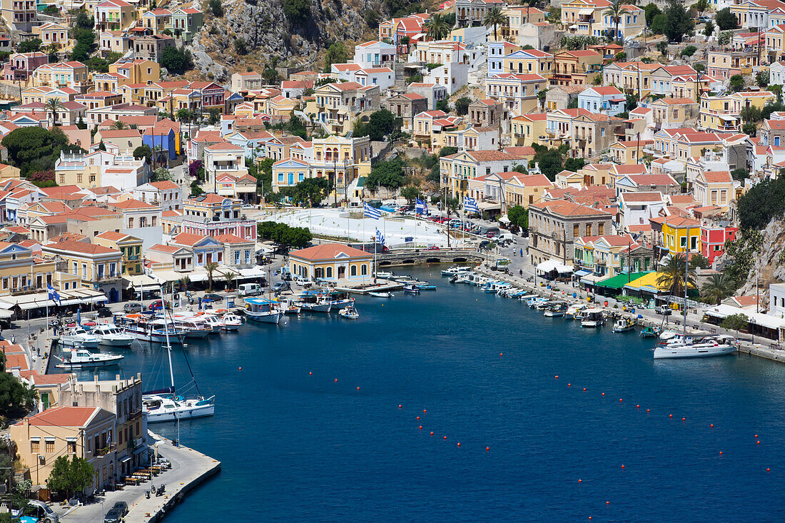 Überblick über das Stadtzentrum von Symi und die am Ufer vertäuten Boote im Yachthafen von Gialos Harbor auf der Insel Symi (Simi); Dodekanes-Inselgruppe, Griechenland