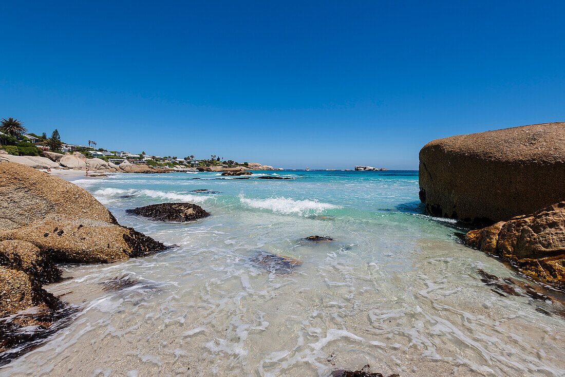 Große Felsbrocken rahmen den Blick auf die Häuser am Strand entlang des felsigen Ufers am Clifton Beach am Atlantischen Ozean ein; Kapstadt, Westkap, Südafrika
