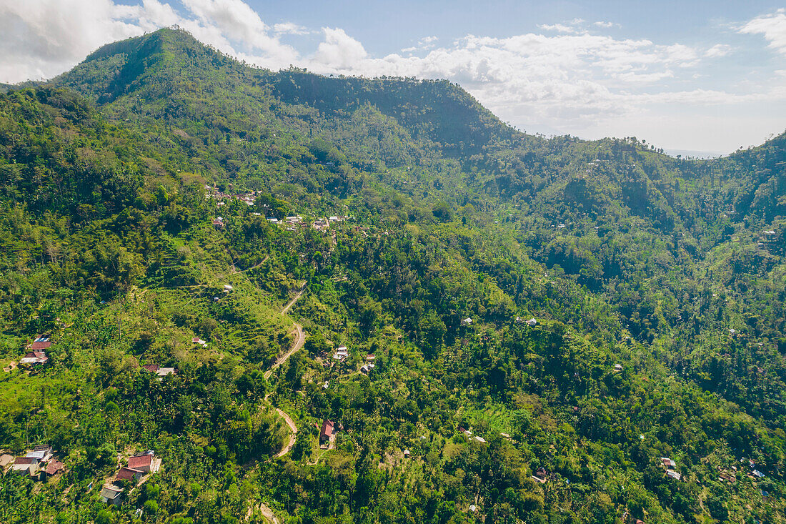 Overview of the mountainside with houses on Mount Abang, with a blue, cloudy sky and lush vegetation; Abang, Kabupaten Karangasem, Bangli Regency, Bali, Indonesia