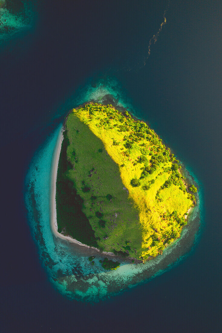 View from directly above of an island in the Komodo National Park, half in sunlight and half in shade, surrounded by turquoise water of the Pacific; East Nusa Tenggara, Lesser Sunda Islands, Indonesia