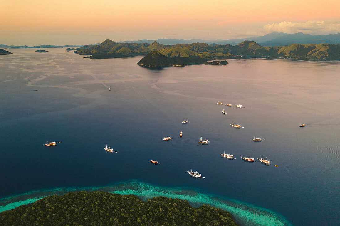 Aerial view of boats moored along the shore of an island in the Komodo National Park, home of the famous Komodo Dragon; East Nusa Tenggara, Lesser Sunda Islands, Indonesia