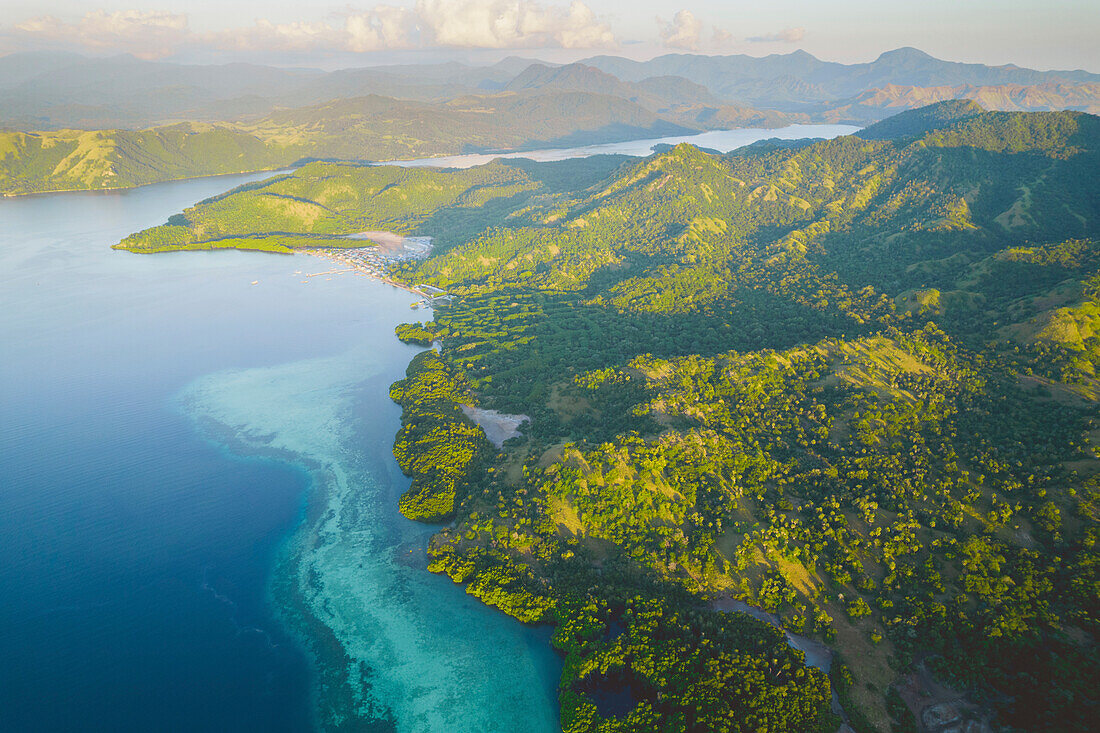 Aerial view of hazy sunlight over the Komodo Islands in the Komodo National Park, home of the famous Komodo Dragon, with a cove with moored boats and a dock; East Nusa Tenggara, Lesser Sunda Islands, Indonesia