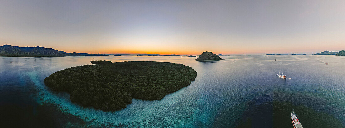 Aerial view of silhouetted islands in Komodo National Park with boats traveling around the ocean waters at sunset; Lesser Sunda Islands, Indonesia