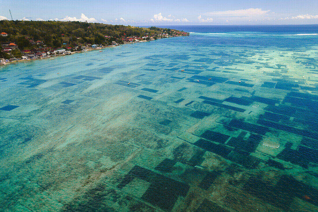 Luftaufnahme der Wasserstraße zwischen Nusa Lembongan und Nusa Ceningan, die kleine Boote zeigt, die über den Unterwasserflecken der Algenzucht im flachen, türkisfarbenen Wasser vertäut sind; Klungkung Regency, Ostbali, Bali, Indonesien