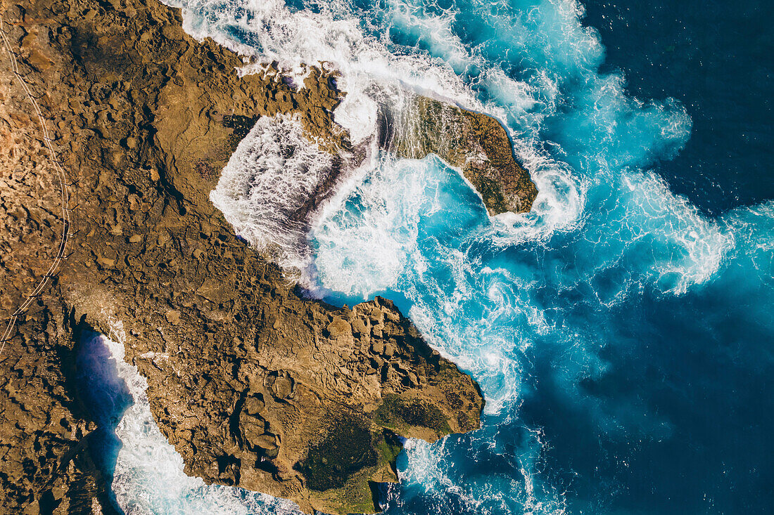 View taken directly above of the rocky coastline of Nusa Lembongan with the turquoise waters of the Bali Sea crashing against the shore; Nusa Islands, Klungkung Regency, East Bali, Bali, Indonesia