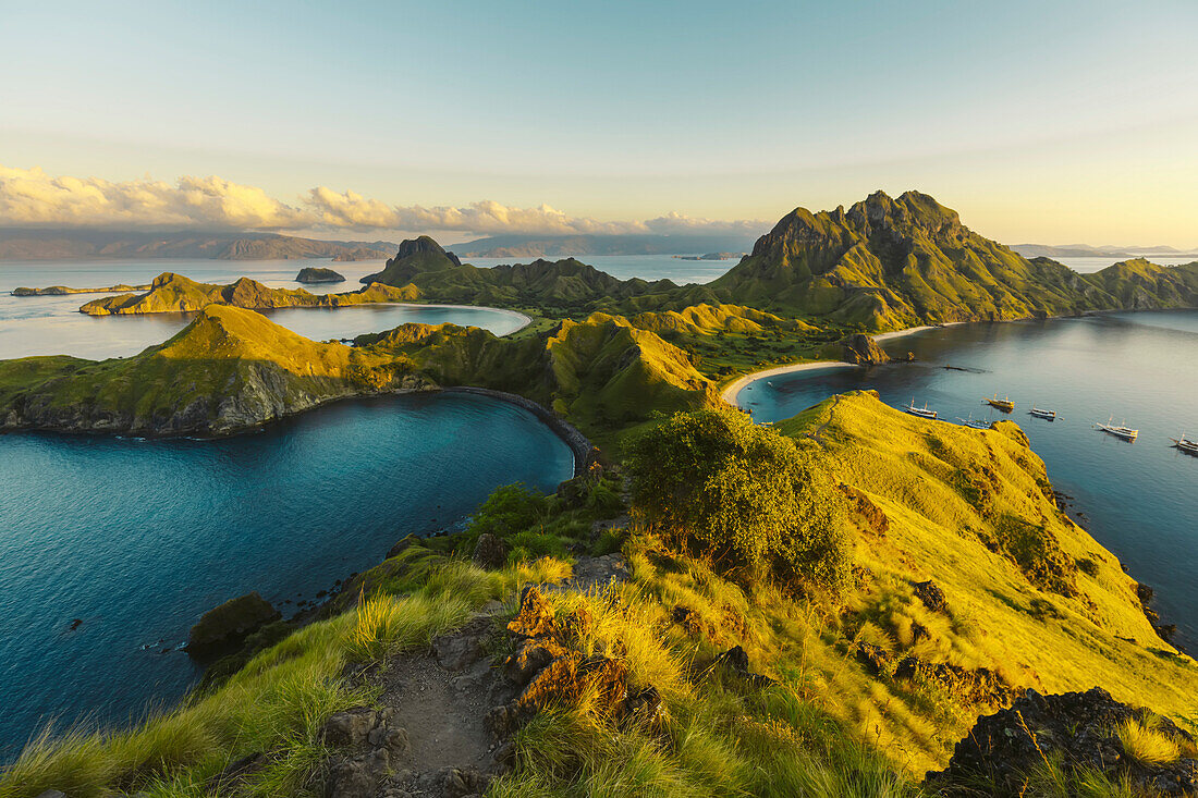 Boats moored in the bay at Padar Island in Komodo National Park in the Komodo Archipelago with sunlit grassy slopes at sunset; East Nusa Tenggara, Indonesia