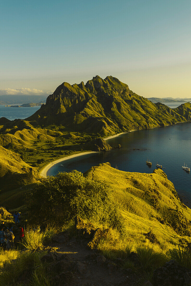 Travelers on hilltop watching the sunset with boats moored in the bay at Padar Island in Komodo National Park in the Komodo Archipelago; East Nusa Tenggara, Indonesia