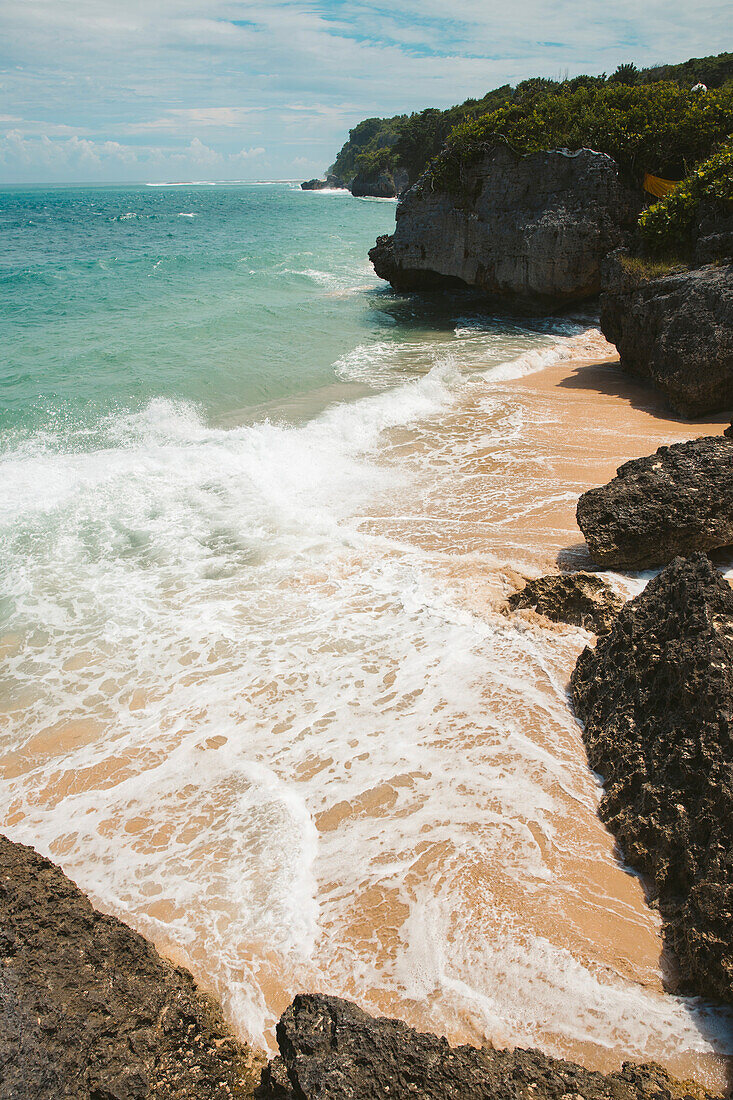 Meereswellen und felsige Küste mit der Brandung, die auf den Sand am Geger Beach im Nusa Dua Resortgebiet rollt; Geger Beach, Badung, Bali, Indonesien