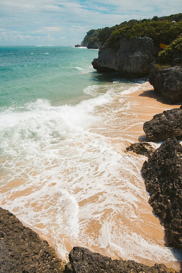 Ocean waves and rocky coast with the surf rolling onto the sand at Geger Beach in the Nusa Dua resort area; Geger Beach, Badung, Bali, Indonesia
