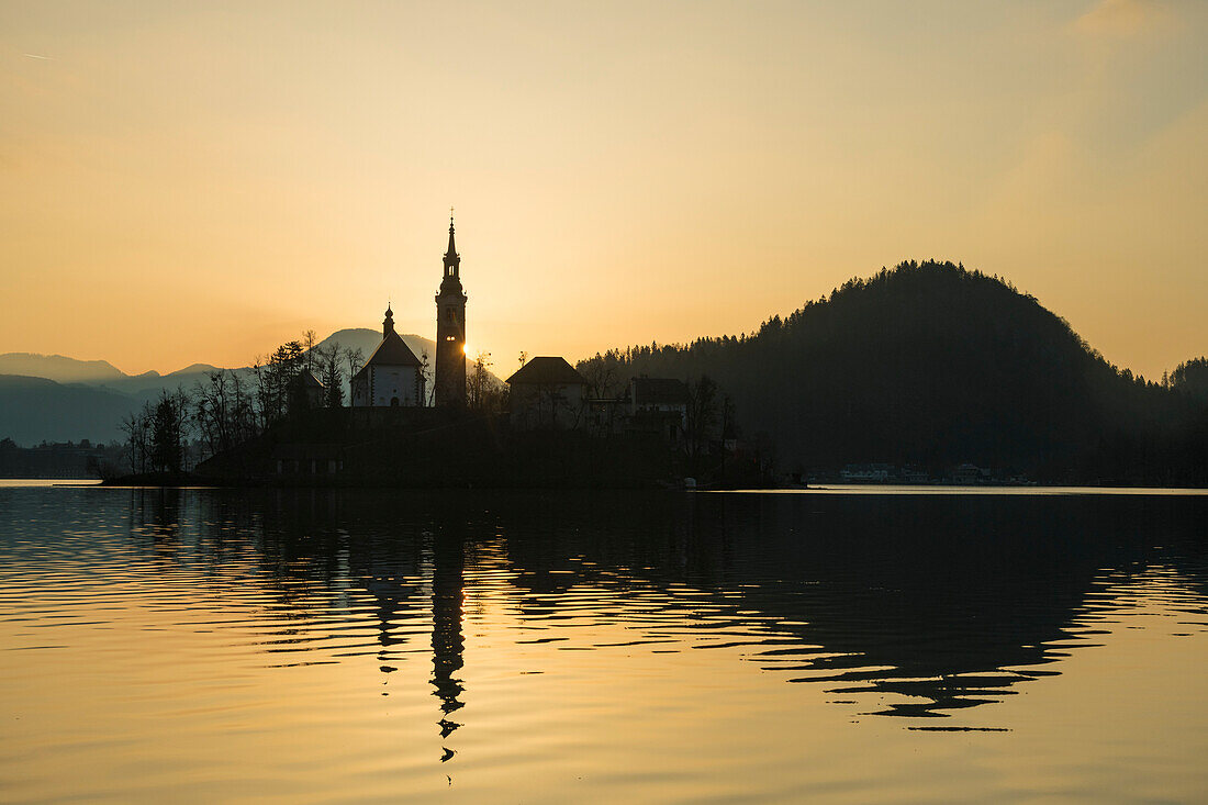 Silhouette der Kirche und anderer Gebäude am Bleder See in der Morgendämmerung; Bled, Slowenien