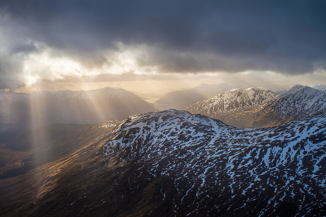 Sonne bricht durch die Wolken über verschneiten Bergen bei Glenfinnan; Schottland, Vereinigtes Königreich