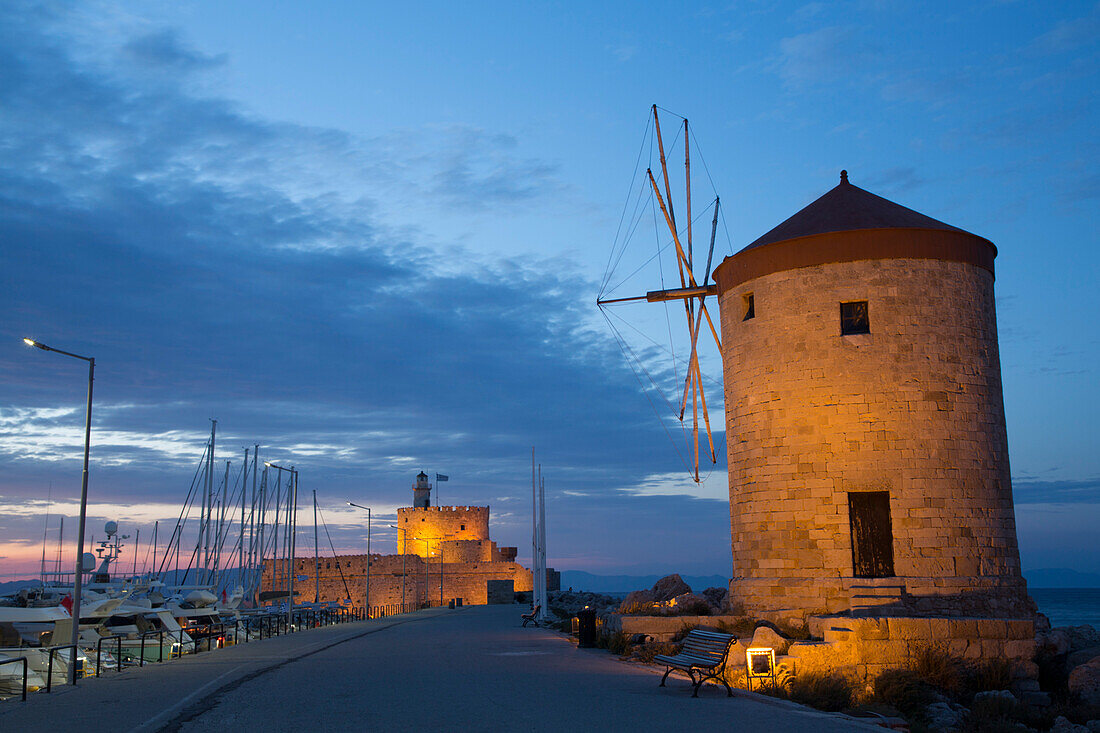 Abend in Rhodos-Stadt mit den Windmühlen von Mandraki entlang der Mole und dem Fort von St. Nicholas im Hintergrund, Mandraki-Hafen, Rhodos; Dodekanes-Inselgruppe, Griechenland