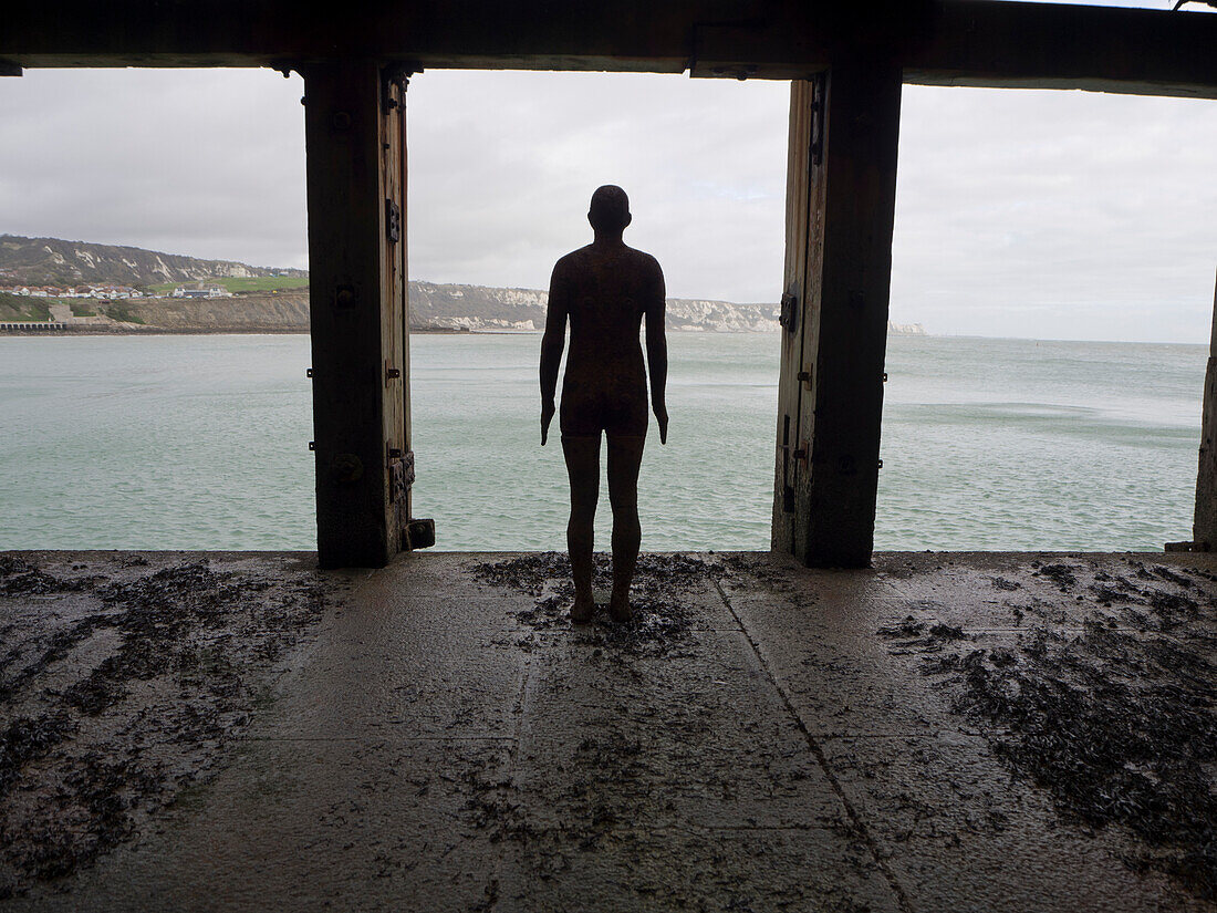 View taken from behind of Antony Gormley's Another Time 1999-2013, cast iron figure, Folkestone Harbour Arm; Folkestone, Kent, England, United Kingdom