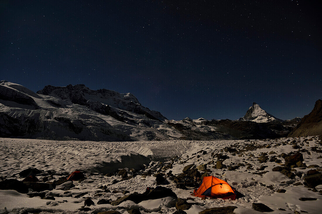 A glowing tent at base camp on the Gorner glacier, with the Matterhorn mountain in the background at night.; Gornergrat, Zermatt, Switzerland.