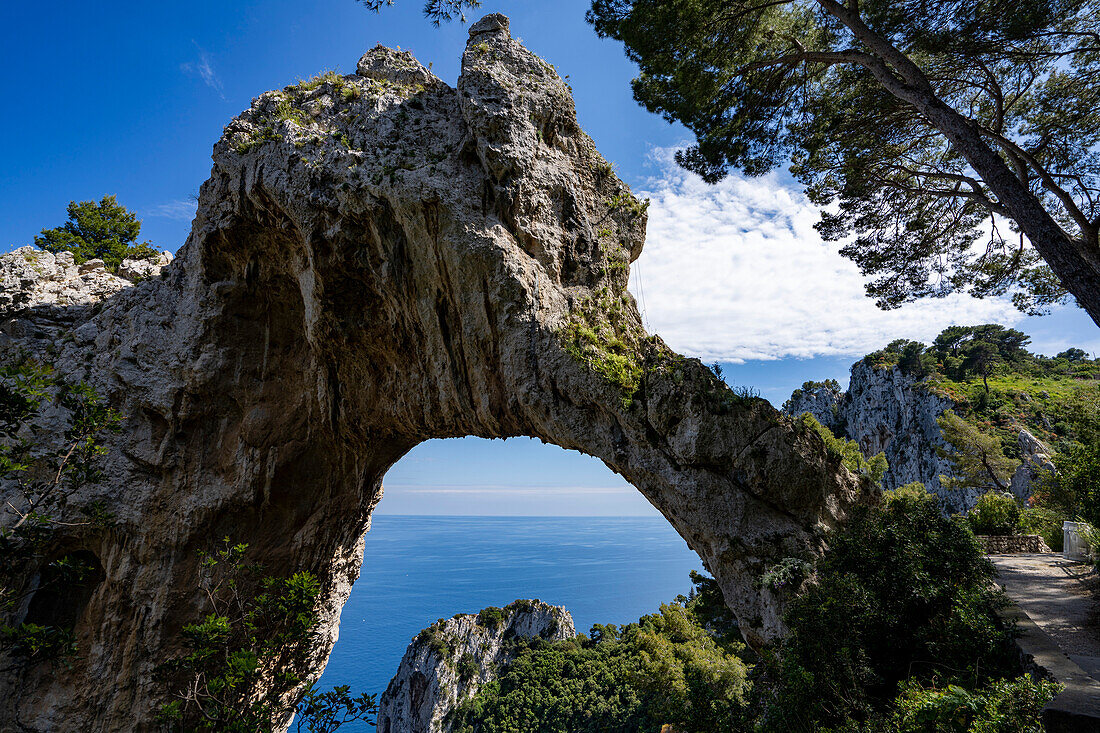 View through the Arco Naturale, a Palaeolithic era limestone arch, remains of a collapsed grotto, 18m high, span of 12m, on the east coast of the Island of Capri; Naples, Capri, Italy