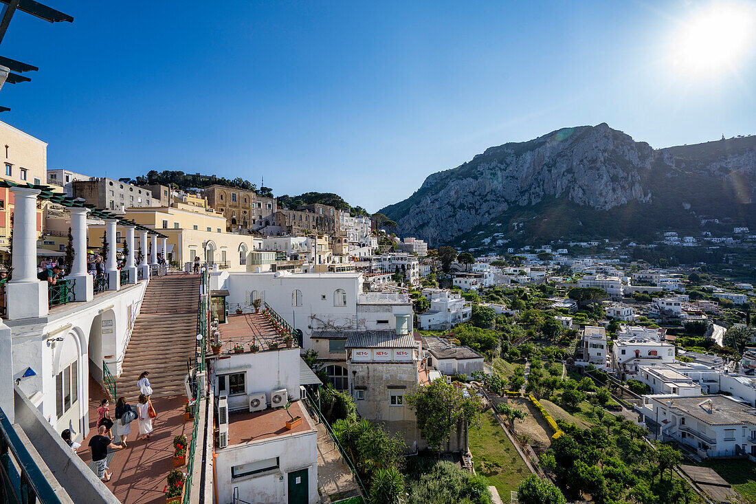 Menschen gehen die Treppe hinauf zu einer Aussichtsterrasse mit Blick auf die Stadt Capri, auf einem sattelförmigen Plateau hoch über dem Meer mit dem Hafen der Insel, Marina Grande darunter; Neapel, Capri, Italien