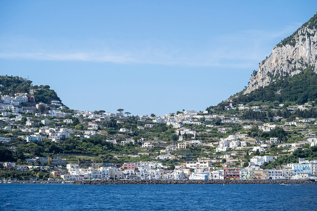 View from the Tyrrhenian Sea looking towards the shore at Capri Town on a plateau like a saddle high above the sea with the island's port, Marina Grande below; Naples, Capri, Italy