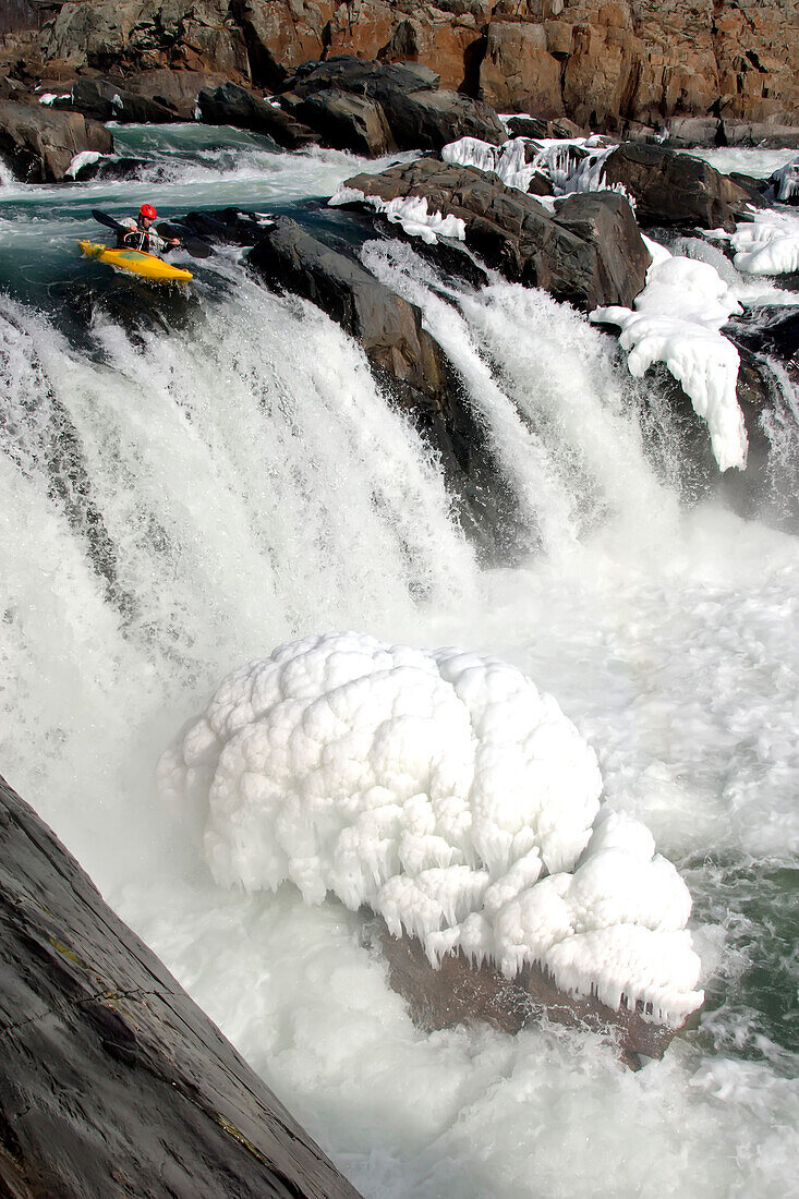 Ein winterlicher Wildwasserkajakfahrer am Rande eines großen Wasserfalls und Eis; Great Falls, Potomac River, Maryland.