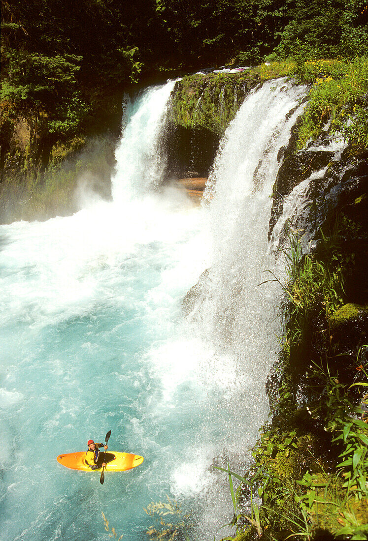 A whitewater kayaker floats beneath a big waterfall.; Little White Salmon River, Washington.