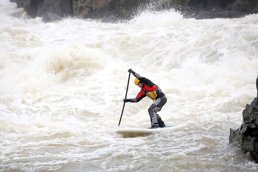 A man on a stand up paddle board runs rapids in the Potomac River.; Great Falls, Maryland.