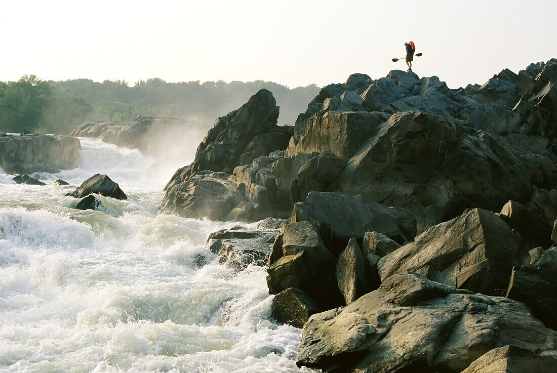 Kayaker carries boat up the rocks of Great Falls on the Potomac River.; POTOMAC RIVER.