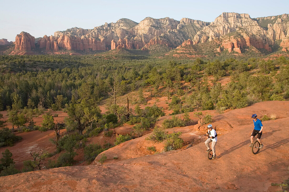 Zwei Männer auf Einrädern fahren auf einem felsigen Bergrücken in der Wüste von Arizona; Sedona, Arizona.