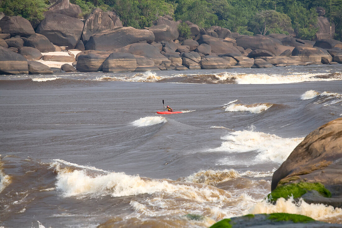 Ein Kajakfahrer paddelt durch einen Wellenzug, der sich einer weiteren Stromschnelle nähert; Unterer Kongo-Fluss, Demokratische Republik Kongo.