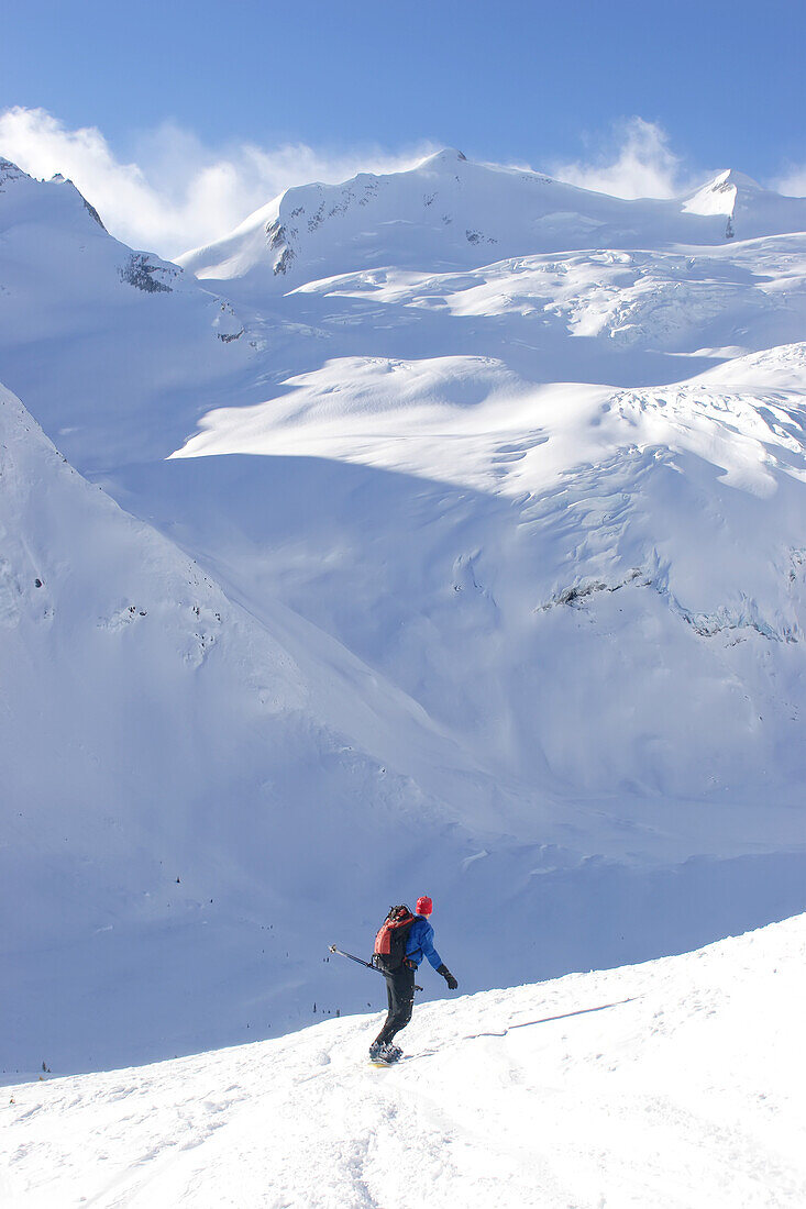 A back country snowboarder descends a snow field toward a glacier.; Selkirk Mountains, British Columbia, Canada.