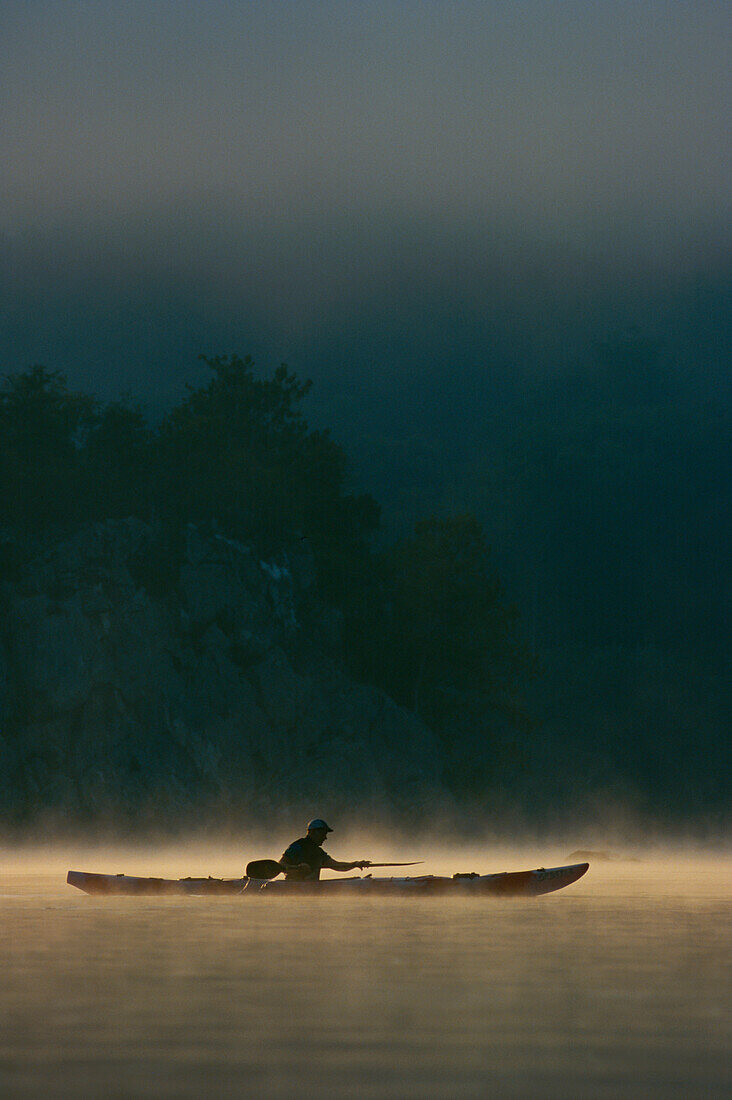 A kayaker paddles through mist rising from the Potomac River at dawn.; Potomac River, Maryland.