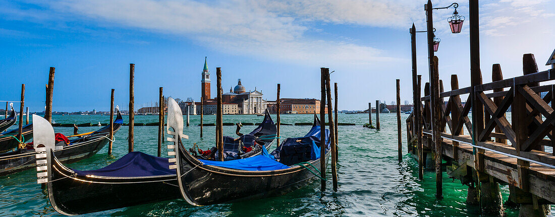 Blau bespannte Gondeln am Ufer und Blick auf den Markusplatz über die Lagune in Venedig; Venedig, Venetien, Italien